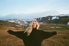 a woman with her arms spread out in front of mountains