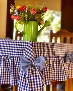 a blue and white checkered table cloth with flowers in a green vase on top