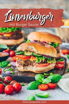 two hamburgers with lettuce and tomatoes on a cutting board next to other burgers