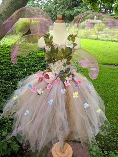 a dress made out of tulle with flowers and leaves on the back, sitting in front of a tree