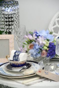 a table set with blue and white plates, silverware and flowers in vases