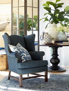 a blue chair sitting in front of a window next to a table with vases on it