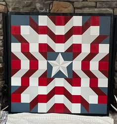 a red, white and blue star quilt is on display in front of a brick wall