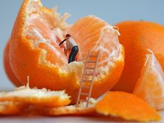 miniature figurines are placed on top of an orange and one is climbing the ladder