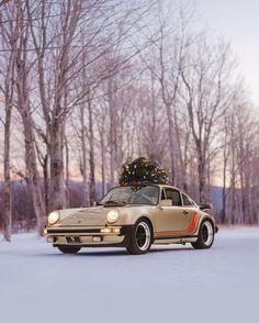 an old car with a christmas tree on the roof parked in the snow next to some trees