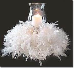 a candle is lit in a glass vase with white feathers on the bottom and inside