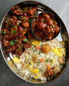 a silver plate topped with rice and meat next to a bowl filled with veggies