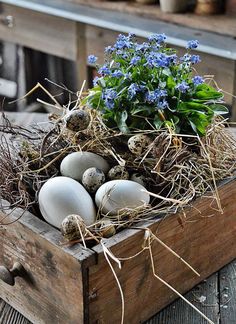 a wooden box filled with eggs sitting on top of a table next to blue flowers