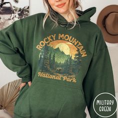 "Show off your love of Colorado's Rocky Mountains and our nation's beautiful National Parks in our Rocky Mountain National Park Hoodie! This hooded sweatshirt is all about embracing the great outdoors, featuring a custom design that showcases the beauty of the Colorado landscape and the towering peaks of the Rockies (complete with a black bear to boot)! The Gildan 18500 50/50 blend fabric has that comfy, lived-in feel, that's like a hug every time you put it on! Now you can take a bit of the Rockies with you wherever you wander! Grab one while you can, and hit the trail! * Product Highlights * This unisex heavy blend hooded sweatshirt is relaxation itself. Made with a thick blend of cotton and polyester, it feels plush, soft and warm, a perfect choice for any cold day. In the front, the sp Cheap Winter Sweatshirt For Hiking, Cheap Winter Hiking Sweatshirt, National Park Shirts, Tennessee Sweatshirt, National Park Sweatshirt, New River Gorge, Hot Springs National Park, New River, Great Smoky Mountains National Park