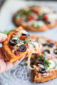 a hand holding a slice of pizza with olives and cheese