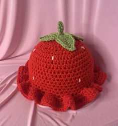 a crocheted red hat with a green leaf on top sitting on a pink surface