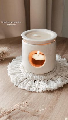 a white candle holder sitting on top of a wooden table next to some dried grass