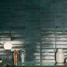 two vases on a table in front of a blue tiled wall