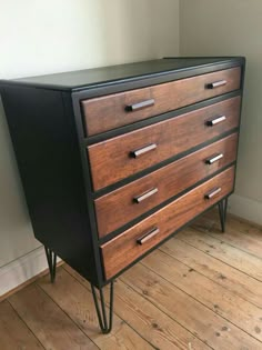 a black and brown dresser sitting on top of a hard wood floor next to a white wall