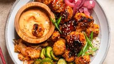 a white plate topped with meat and veggies next to a bowl of sauce