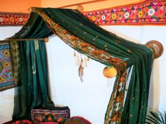 a canopy bed with green drapes and colorful decorations on the wall behind it,