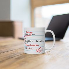 a coffee mug with writing on it sitting on a wooden table next to a laptop