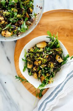 a bowl filled with green vegetables on top of a wooden cutting board next to a glass bowl