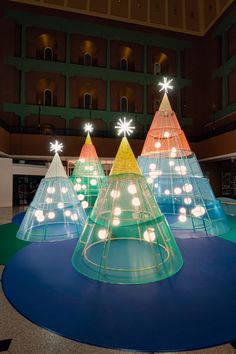 three brightly lit christmas trees on display in a large room with circular blue flooring