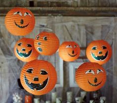 orange lanterns with faces hanging from strings in front of a wooden wall and pumpkins