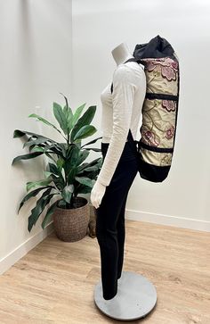 a mannequin with a backpack on it's back stands in front of a potted plant