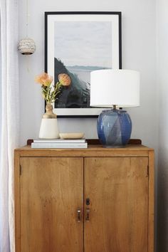 a blue vase with flowers on top of a wooden dresser next to a white lamp