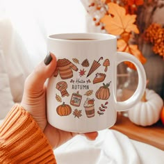 a woman holding a white coffee mug with autumn icons on it and an orange pumpkin in the background