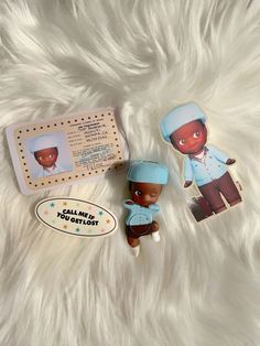 two small dolls sitting next to each other on a white fur covered surface with an information card and sticker