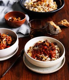 three bowls filled with food sitting on top of a wooden table next to plates and utensils