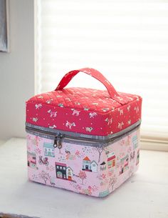 a pink and red lunch box sitting on top of a table next to a window