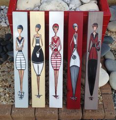 three wooden signs depicting women in different dresses and haircuts, one is painted red the other is white