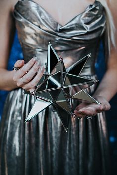 a woman in a silver dress holding an origami star brooch on her chest