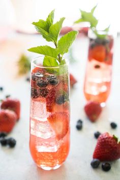 two glasses filled with fruit and ice sitting on top of a white table next to strawberries