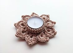 a crocheted candle holder with a lit candle in it on a white surface