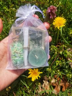 a hand holding a plastic bag filled with money and green candles next to yellow flowers