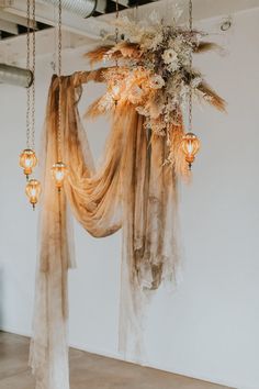 an arrangement of flowers is hanging from the ceiling in front of a white wall with sheer curtains