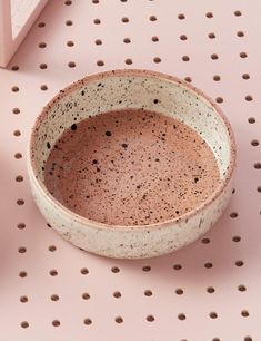 a white and brown bowl sitting on top of a pink table next to a cup