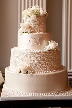 a three tiered wedding cake with white flowers on the bottom and monogramming