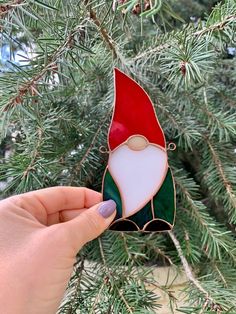 a hand holding a glass ornament in front of a pine tree with green and red leaves