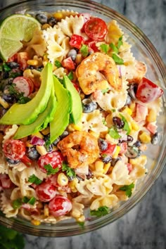 a glass bowl filled with pasta salad topped with shrimp, avocado and tomatoes