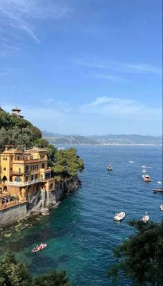 boats are floating on the water in front of some houses and cliffs with trees around them