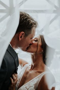 a bride and groom kissing in front of a white curtain