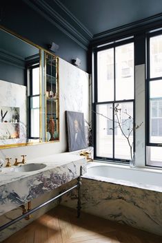 a bathroom with marble counter tops and bathtub in front of two large windows that look out onto the street