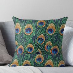 a green and blue peacock print pillow sitting on top of a couch next to pillows