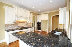 a large kitchen with marble counter tops and white cabinets, along with hardwood flooring