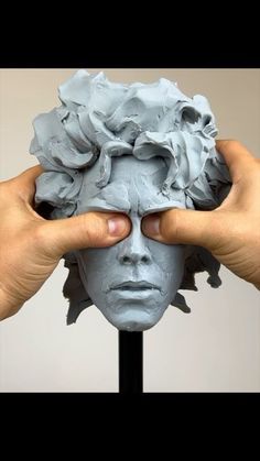 two hands are holding up a clay face