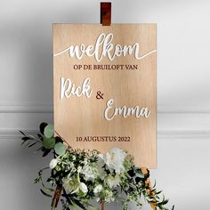 a wooden sign that says welcome to the bride and groom with flowers in front of it