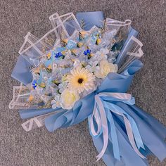 a bouquet of flowers is wrapped in blue and white ribbon on the ground with other items around it