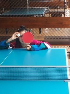 a woman holding a ping pong paddle on top of a blue ping pong table