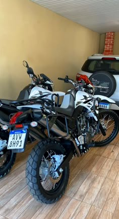 two motorcycles parked next to each other in a room with a car and truck behind them